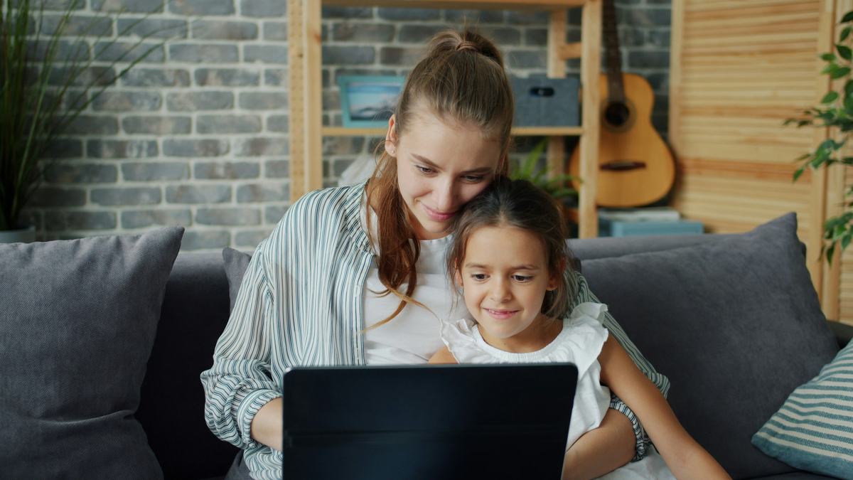 Working mother juggling life admin and personal tasks working on her laptop with her daughter